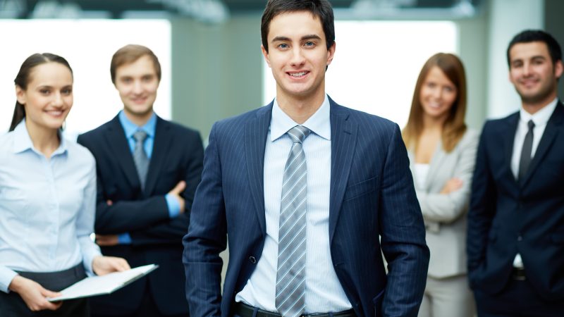 Man smiling in suit with team members stood around him