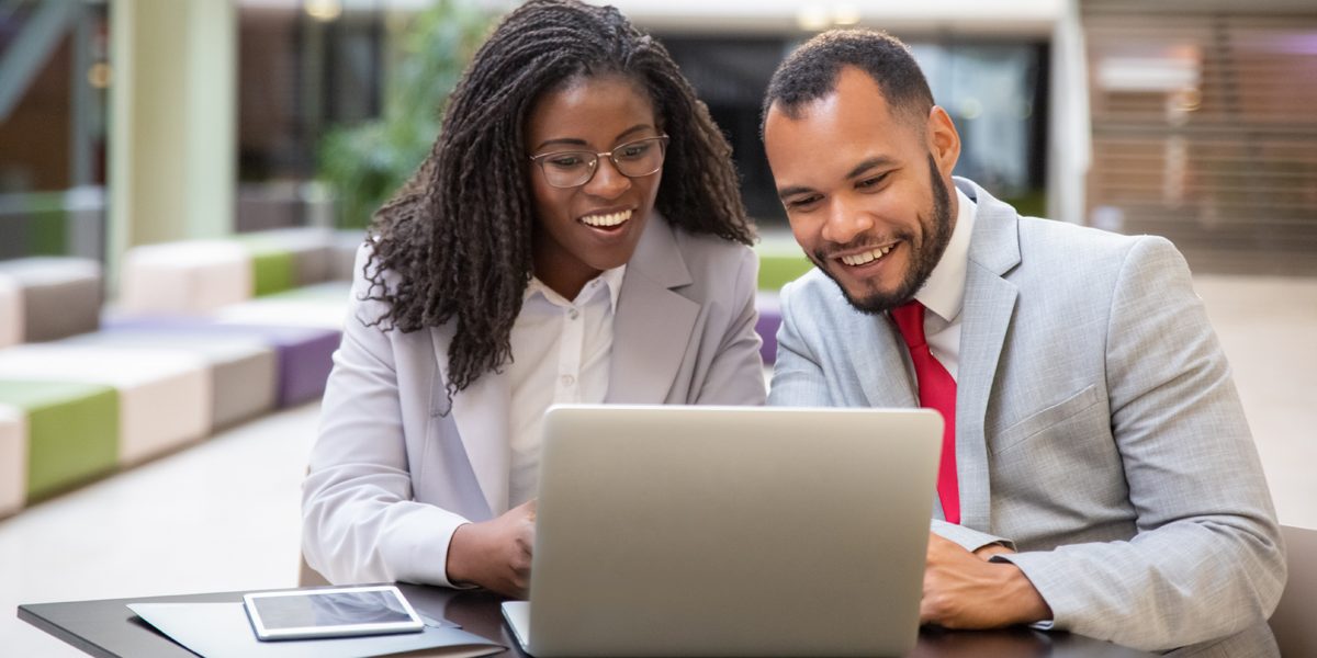 Man and woman sat at desk on laptop smiling in suits